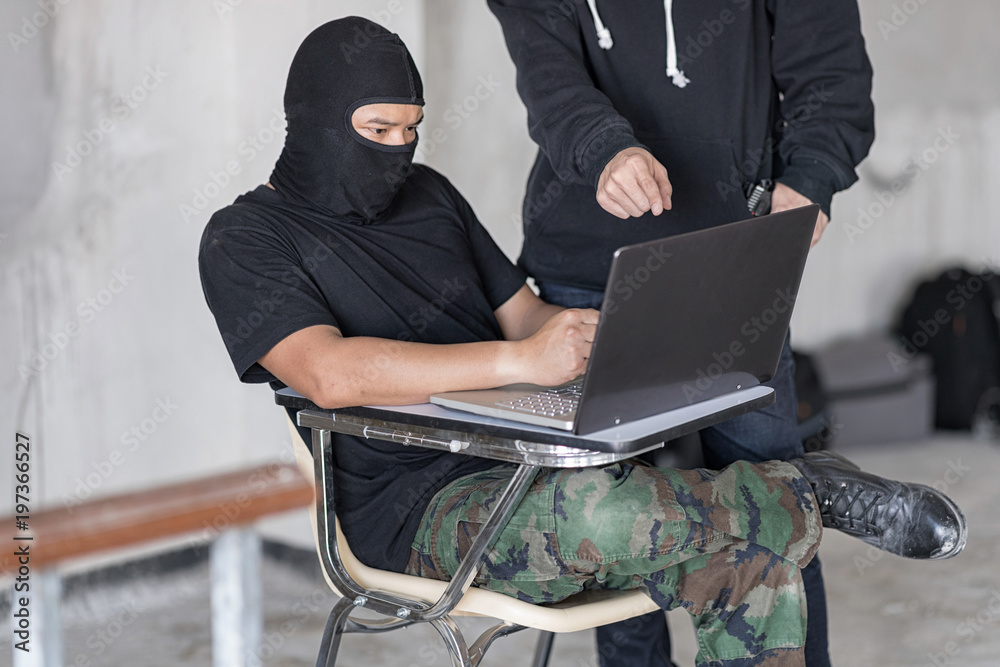 Two hackers are using laptop, Hacker in the camouflage pant is sit with  one's legs crossed