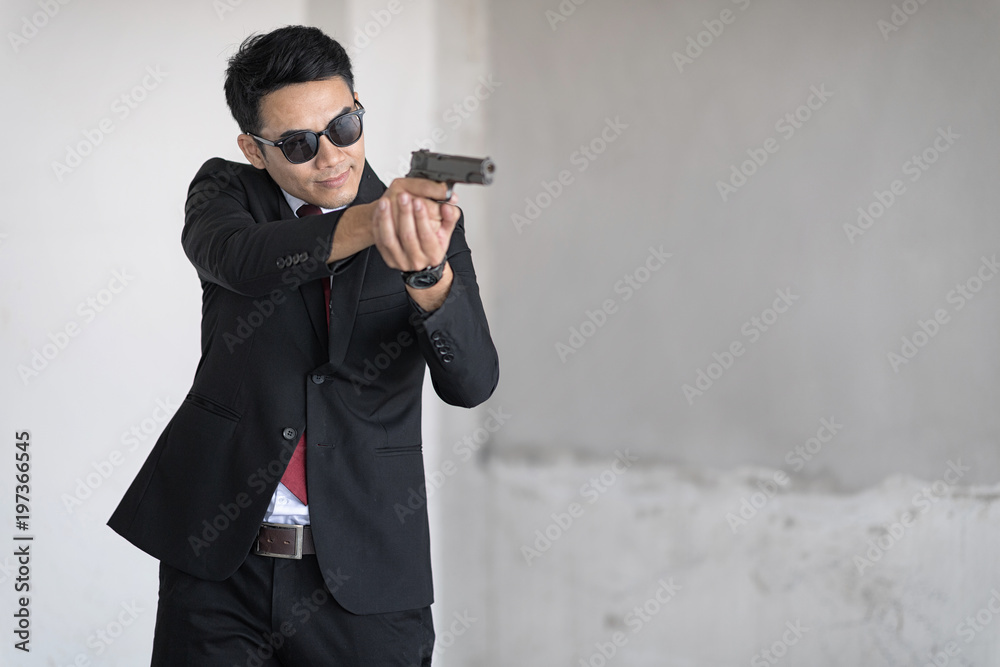 Handsome man with sunglass is aim the gun. Selective focus at his face. - obrazy, fototapety, plakaty 