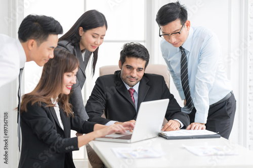 A confident business team of mixed ages using labtop computer thegether for meeting in a modern office. They are discussing ideas for their business development.In selective focus on face.