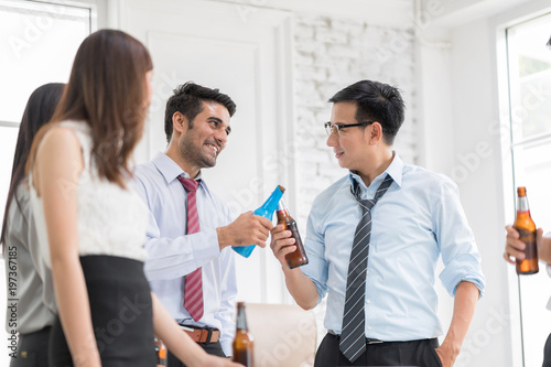 The colleague celebrating after work.Standing around wooden table lifting their beer bottles in work place office.Smiling and talking.Motion blur movement,In selective focus on people face.