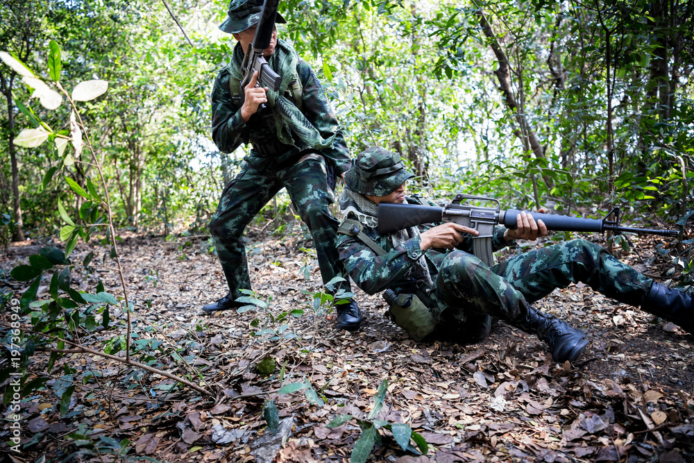 Asian army soldier with weapon during rescue operation evacuate injured fellow at across the deep forest.