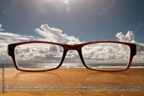 Brille auf einem Tisch liegend mit blauem wolkigen Himmel über dem Meer im Hintergrund © OFC Pictures