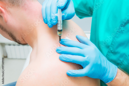 Close up Neurologist doctor makes an injection therapy (blockade) into trapezium muscle of male patient. Alternative pain treatment concept. Selective focus, space for text. photo
