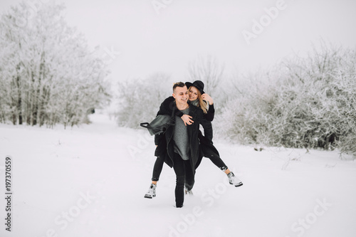 Young and cheerful couple walk through the snow in winter
