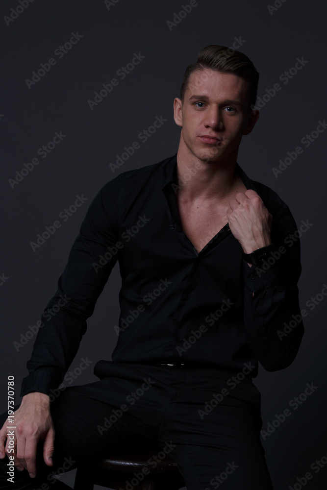 Fototapeta premium a guy in a black shirt and black pants sits on a dark chair, on a gray background