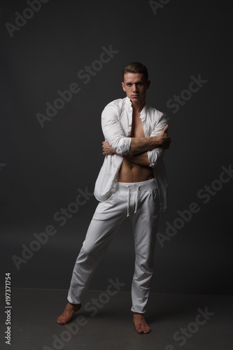 a guy with a naked torso, in white pants, and in a white shirt, stands on a gray background