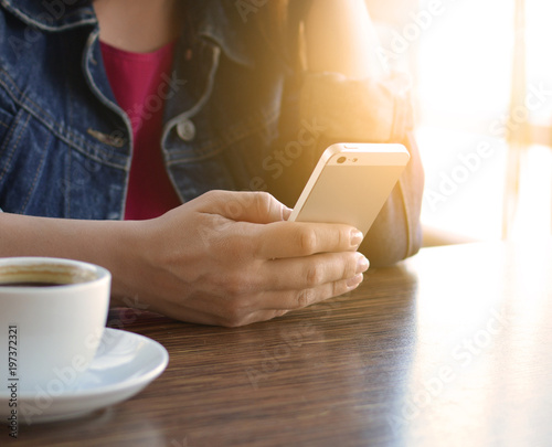 A brunette girl in a denim jacket is eating lunch in a cafe and using her phone. Communication through messenger. Smartphone. Casual loose clothing