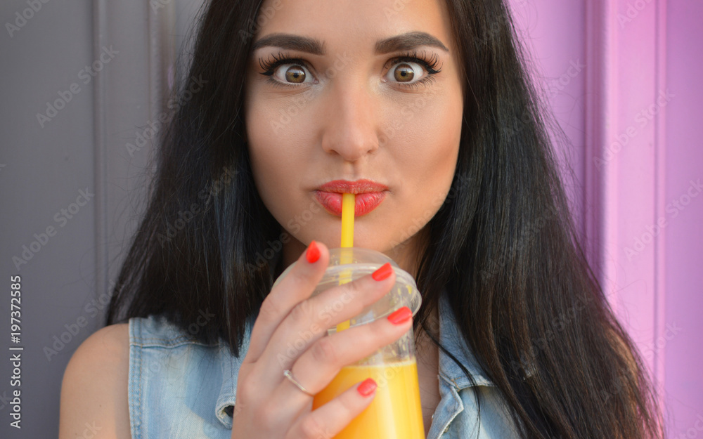 Healthy lifestyle. The brunette girl drinks fresh juice through a straw. Widely open eyes. Orange fresh. Vitamins. Surprise. Close-up portrait. Delicious Healthy lifestyle. The brunette girl drinks fresh juice through a straw. Widely open eyes. Orange fresh. Vitamins. Surprise. Close-up portrait. Delicious