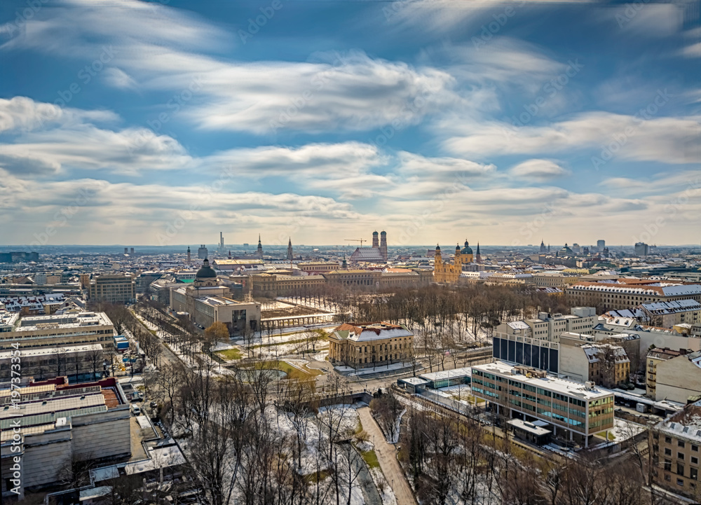 München von oben als kleine Langzeitbelichtung als urbanes Aerial/Luftbild mit weichen, sanften Wolken an einem sonnigen Frühlingstag mit etwas Schnee vom Restwinter