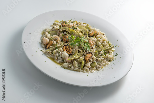 Round white dish of risotto with artichokes and seafood