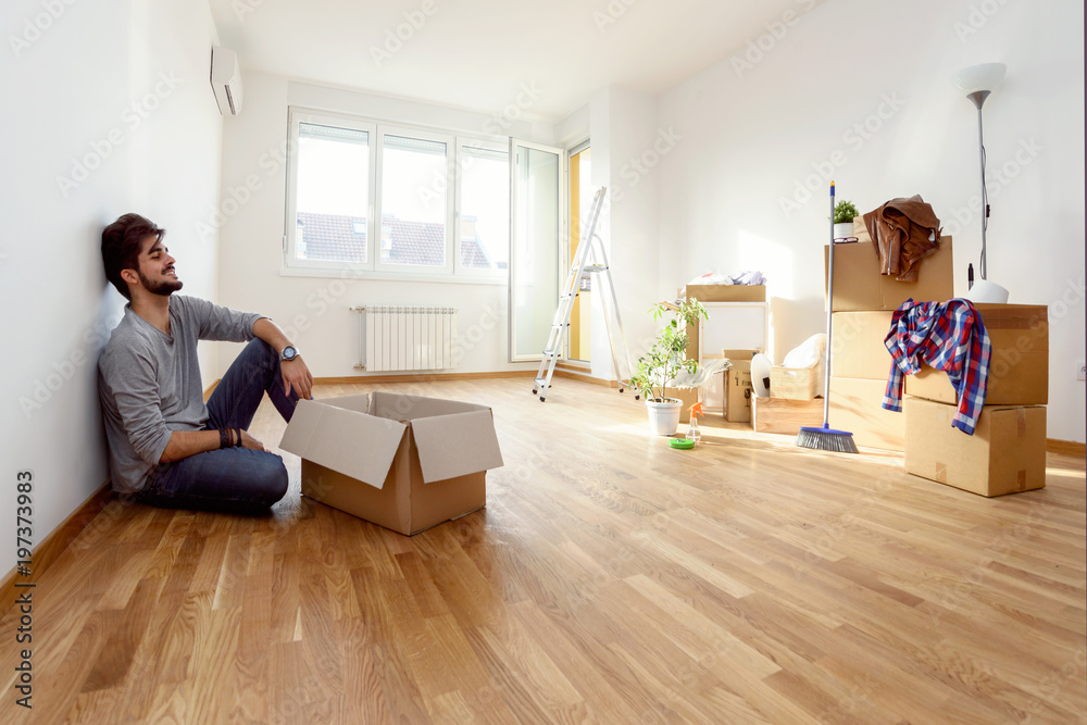 Obraz premium Happy young man just moved into new home unpacking boxes sitting on the floor