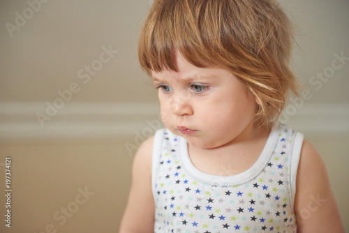 Portrait of cute adorable blonde Caucasian smiling baby child girl sitting on floor indoor, fairy tale sun light from above behind