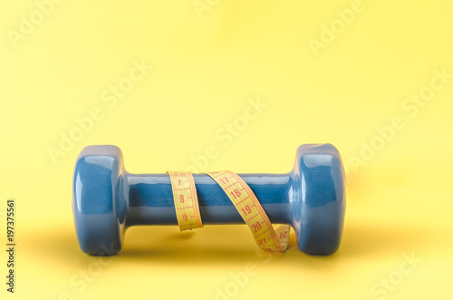 blue dumbbell with yellow centimeter/blue dumbbell with centimeter on a yellow background. Copy space photo