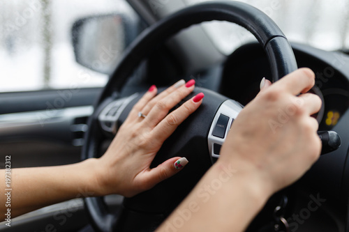 Close up of woman hand pressing the horn button while driving a car through the road. Woman driving a car with hand on horn button. Closeup woman hand holding steering wheel and honking the horn