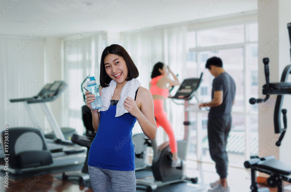 young happy smile asian woman slim body with towel drinking water while resting after workout for good healthy in fitness gym, bodybuilder, healthy lifestyle, exercise and sport training concept