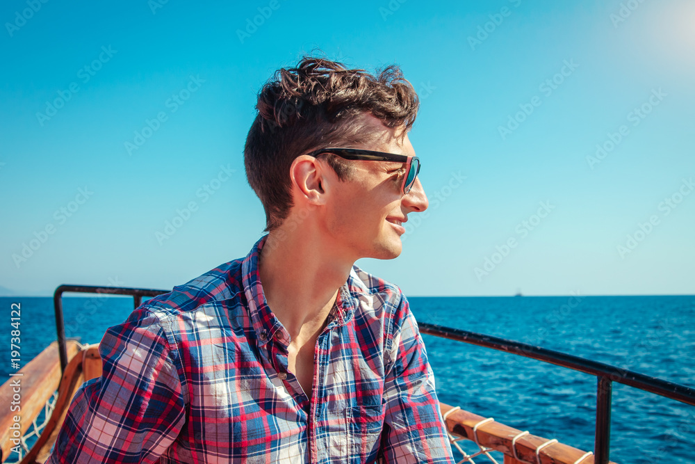 Fototapeta premium Young man enjoys the seaside view on a wooden yacht