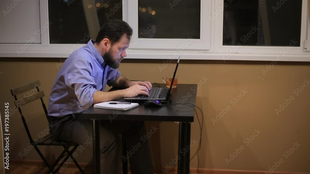a tired businessman works late in the evening with a laptop in the office and composes a financial report. a tired businessman works late in the evening with a laptop in the office and composes a financial report.