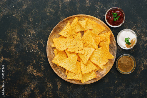 Nachos corn chips with variety of sauces on rustic dark background. The view from the top, place for text.