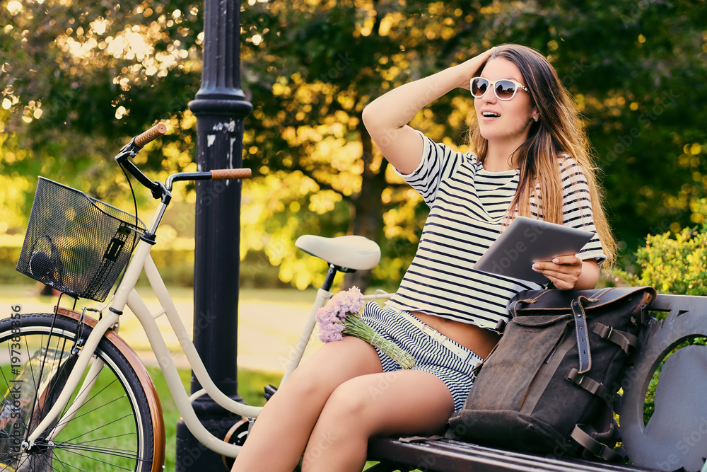 Obraz premium Portrait of an attractive brunette sits on a bench with bicycle
