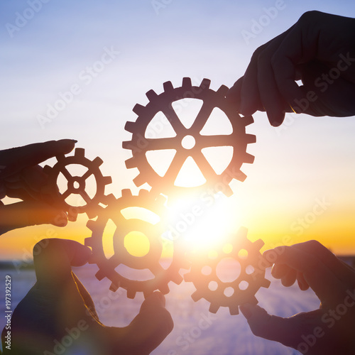 Four hands collect the gear from the gears of the details of the puzzles. against the background of sunlight. Concept business idea. Teamwork