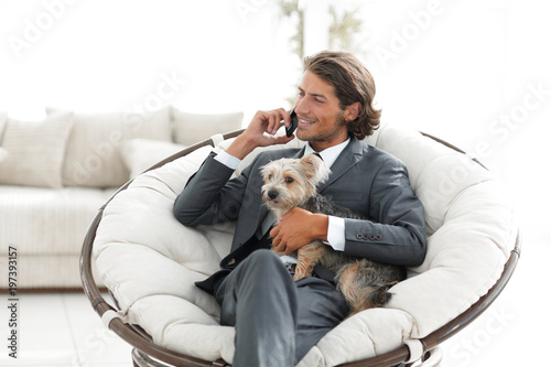 businessman holds his pet and talks on the smartphone while sitting in a comfortable chair © ASDF
