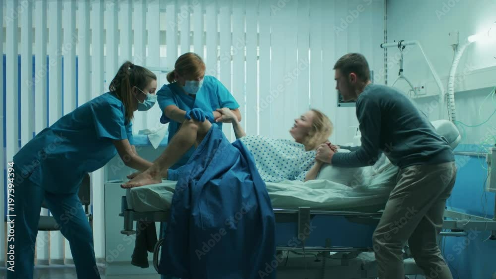 In the Hospital Woman in Labor Pushes to Give Birth, Obstetricians Assisting, Husband Supports Her by Holding Hand. Shot on RED EPIC-W 8K Helium Cinema Camera. In the Hospital Woman in Labor Pushes to Give Birth, Obstetricians Assisting, Husband Supports Her by Holding Hand. Shot on RED EPIC-W 8K Helium Cinema Camera.