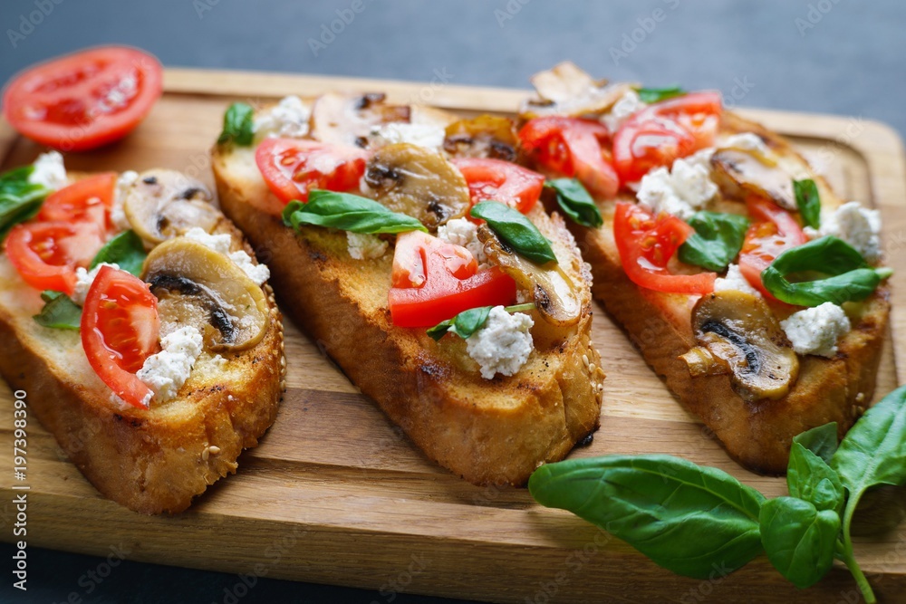 Delicious traditional Italian antipasti bruschetta with chopped tomatoes, ricotta and basil on wooden board, close up Delicious traditional Italian antipasti bruschetta with chopped tomatoes, ricotta and basil on wooden board, close up