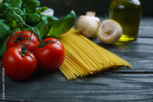 Pasta cooking ingredients. Raw spaghetti, tomatoes, basil, olive oil, mushrooms and spices on rustic wooden table. Italian cuisine food background concept