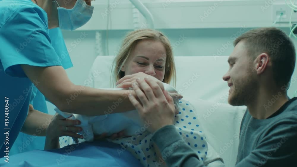 In the Hospital Midwife Gives Newborn Baby to a Mother to Hold, Supportive Father Lovingly Hugging Baby and Wife. Happy Family in the Modern Delivery Ward. Shot on RED EPIC-W 8K Helium Cinema Camera.