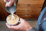 Barista pouring steamed milk into coffee cup making latte art