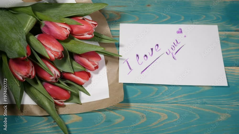 Top view of a I Need You message note and Tulips flowers bouquet on a wooden table. Love relationship concept. Saint Valentines Day. Shot in 4 k Top view of a I Need You message note and Tulips flowers bouquet on a wooden table. Love relationship concept. Saint Valentines Day. Shot in 4 k