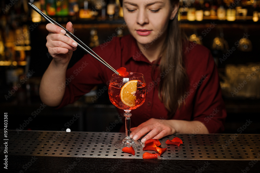Woman barman decorating a glass of Aperol syringe cocktail with rose petals