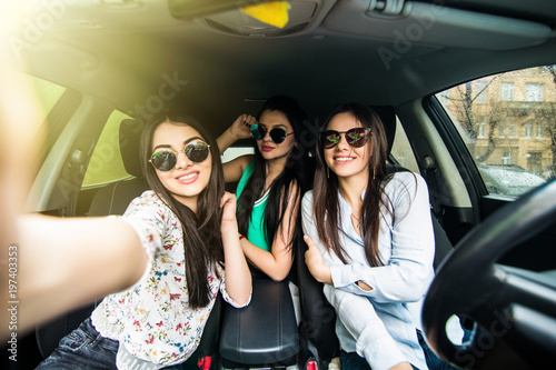 three young cheerful women making selfie and smiling while sitting in car together
