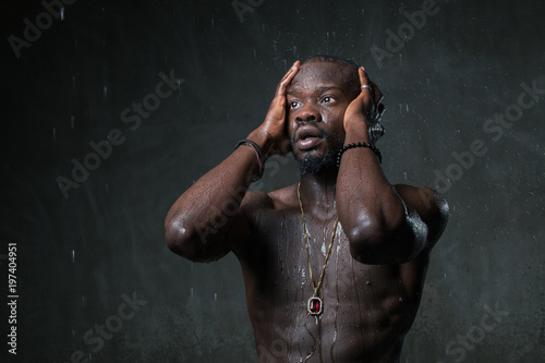 Fit strong physique African American young man under the rain near gray concrete cement wall. Street style concept. Dramatic emotions mood concept. Copy space background.