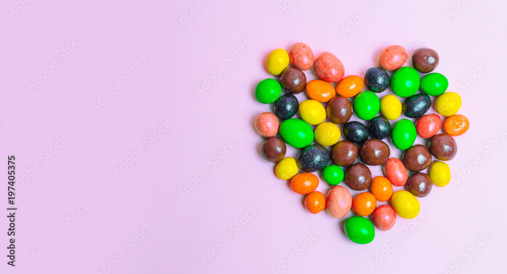 Obraz premium heart of sweets, colorful candies on a pink background, sweet food. the concept of love. banner. copy space