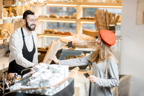 Woman buying baguette in the small and cozy coffee house with bakery products