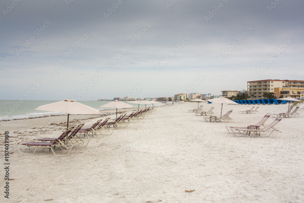 Beach chairs and umbrellas on a Florida Beach with high rise condominiums in the distance on a cloudy day. Beach chairs and umbrellas on a Florida Beach with high rise condominiums in the distance on a cloudy day.