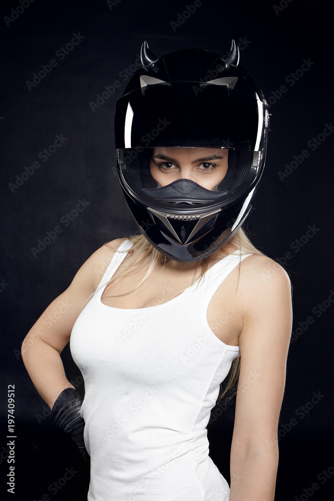 Vertical image of gorgeous stylish young fit female with athletic body posing in studio, wearing white sleeves t-shirt and black protective helmet, having confident look. Style and fashion
