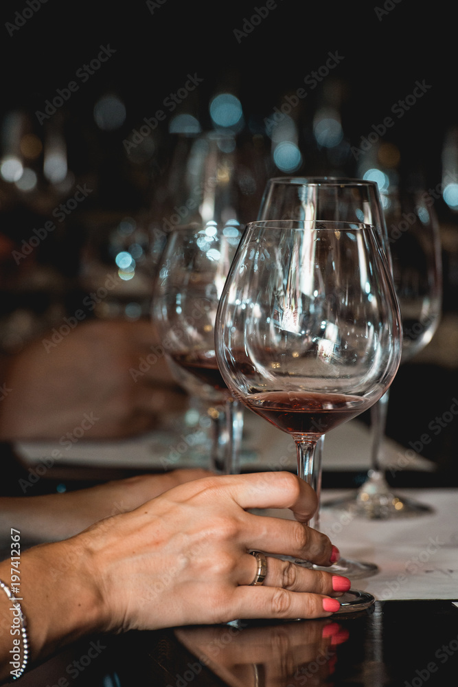 woman holds glass of red wine. people consider the color of the wine and try how it smells in different glasses