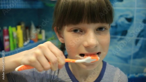 Little child girl face portrait brushing her teeth with a toothbrush in bathroom in the morning photo