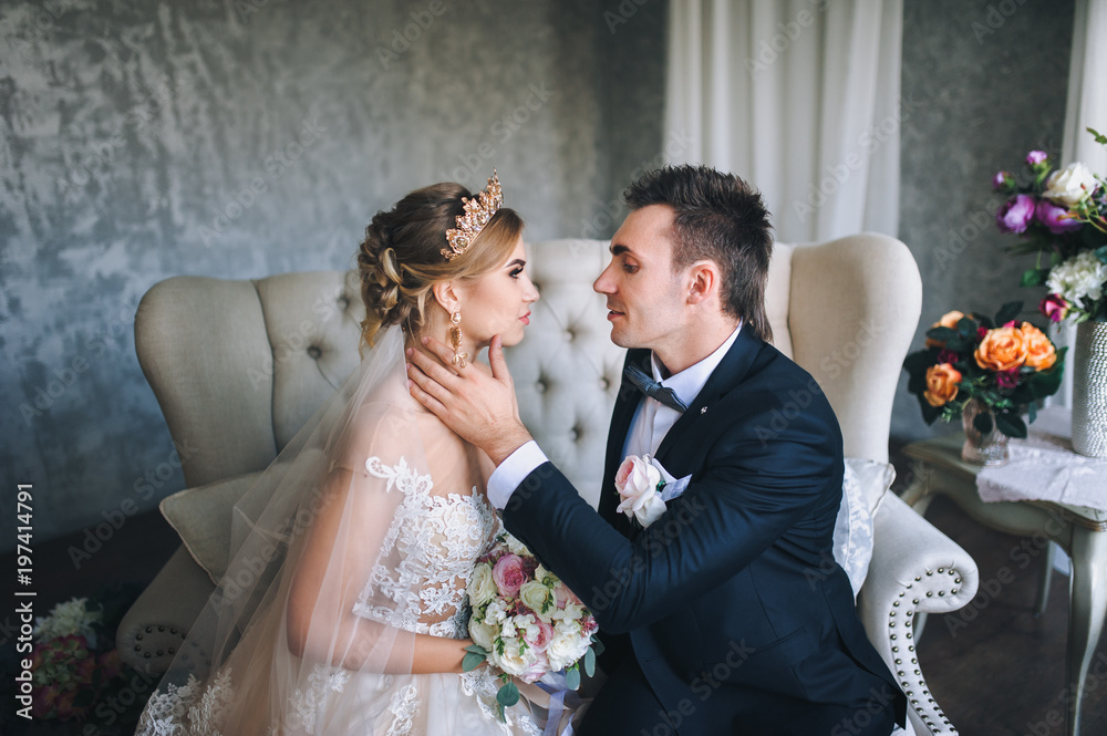 The groom kisses his beautiful bride. Interior. Sofa. Desire to kiss.