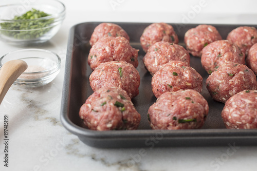 Raw meat balls prepared and ready to be baked on a sheet pan with seasonings on the side