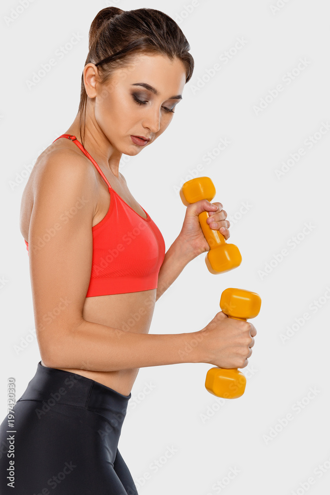 A sporty girl in a red T-shirt is holding yellow dumbbells A sporty girl in a red T-shirt is holding yellow dumbbells
