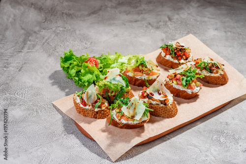 Italian bruschetta with salmon, tomatoes, cheese and basil pesto on a grey concrete or stone background.
