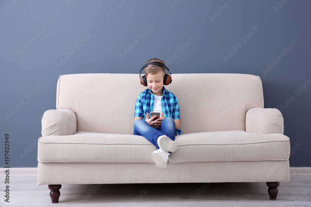 Cute little boy listening to music on sofa, indoors