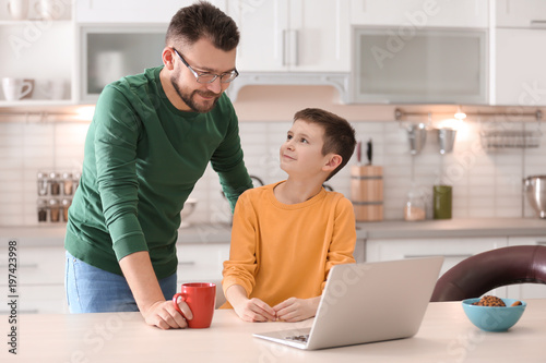 Little boy and his dad using laptop in kitchen © New Africa