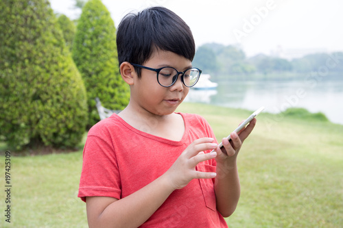 Asian boy in red t-shirt dress hold mobile phone on hand with  garden scene