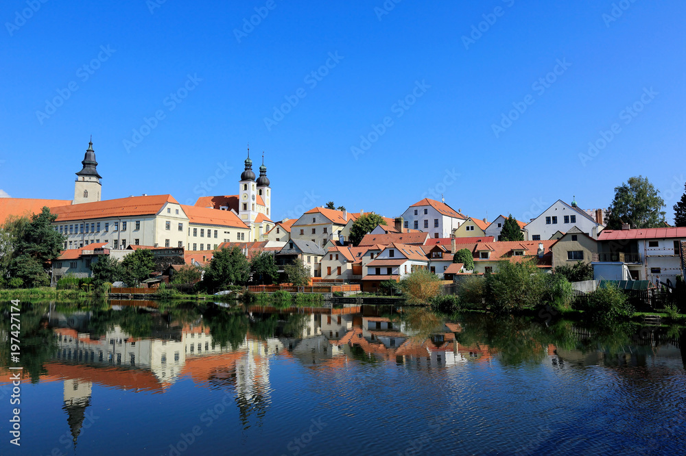 A fairy tale castle and old town with beautiful mirror reflections on smooth lake water under clear blue sky in Telc, a UNESCO world heritage site in Czech Republic, Europe 