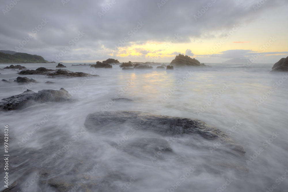 Golden rays of the rising sun light up the rocky beach at Wai'ao, Yilan, Taiwan (Long Exposure Effect)~ Scenery of a beautiful beach illuminated by the first rays of morning sunshine at Ilan, Taiwan  