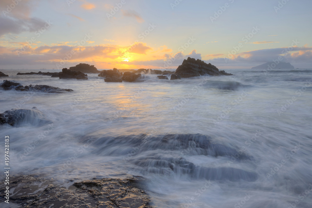 Golden rays of the rising sun light up the rocky beach at Wai'ao, Yilan, Taiwan (Long Exposure Effect)~ Scenery of a beautiful beach illuminated by the first rays of morning sunshine at Ilan, Taiwan  